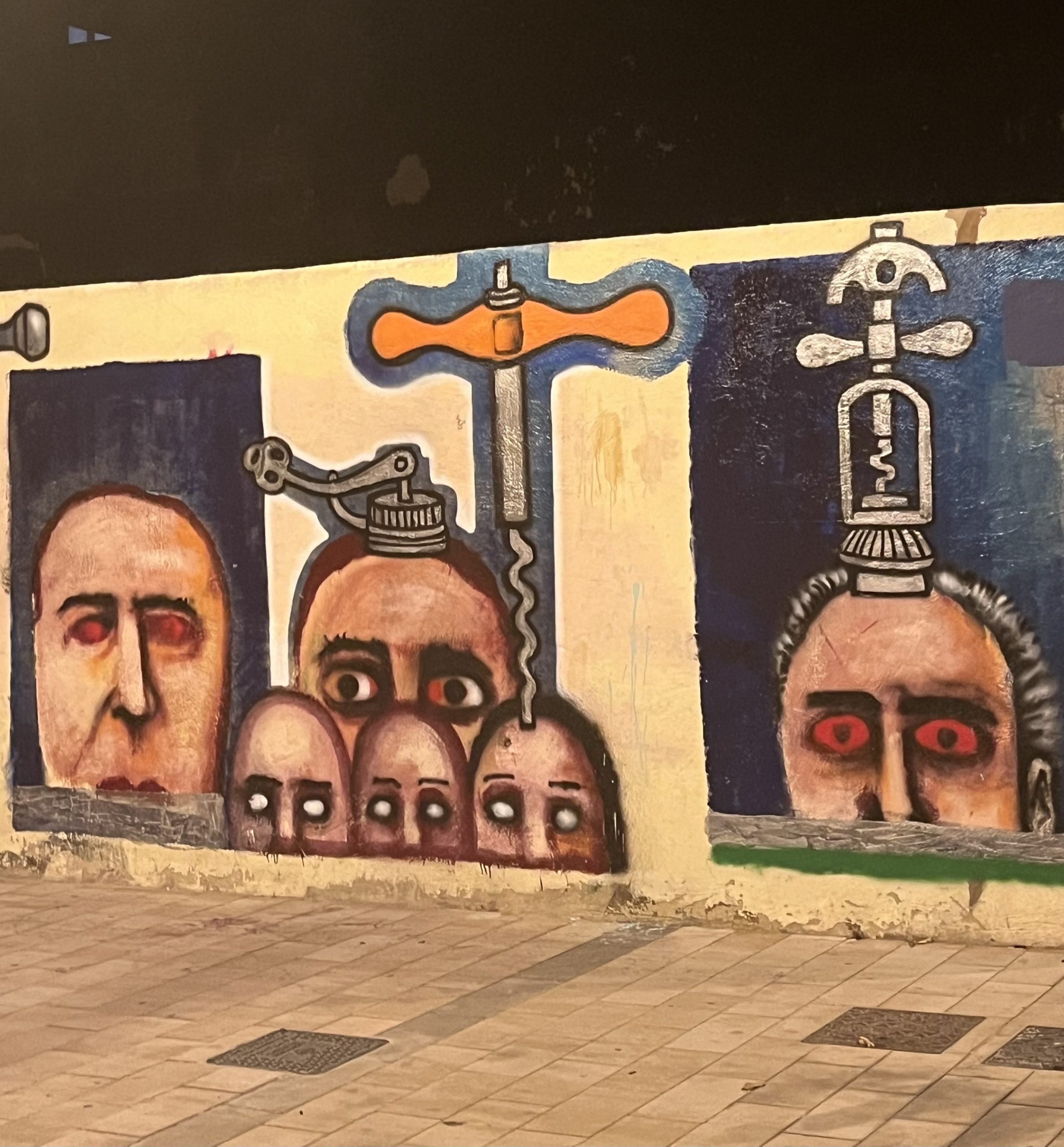 A street mural in the Cabanal area, Valencia large male faces some with bloodshot, some wide-open eyes stare from the walls there’s a dagger in the mix and what looks like a religious vessel on one of the heads