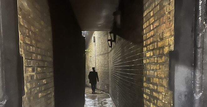A silhouette figure at the end of a dark wet brick alleyway